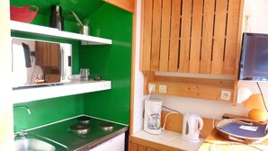 A compact kitchen with a green wall, wooden cabinets, a sink, a stove, and a microwave.
