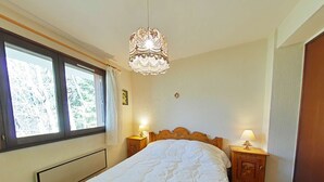 Une chambre à coucher avec un grand lit, deux tables de chevet avec des lampes, une fenêtre avec des rideaux et un lustre.