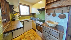 Une cuisine compacte équipée d’un lave-vaisselle, d’une cuisinière et d’une fenêtre laissant entrer la lumière naturelle.