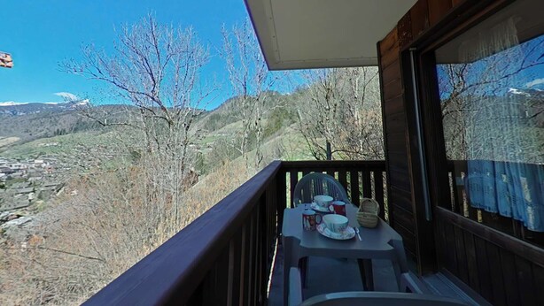 Un balcon avec une table dressée pour deux personnes, donnant sur une vallée bordée d’arbres et sur des montagnes lointaines.
