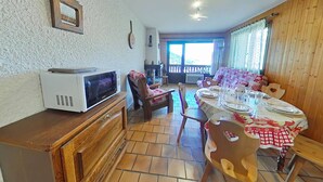 Un coin repas avec une table en bois dressée pour quatre personnes, un four à micro-ondes posé sur un comptoir en bois, et une vue sur l’extérieur par une fenêtre.