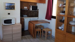 Ett kompakt kök med mikrovågsugn, kylskåp, träskåp och en matplats med bord och stolar.