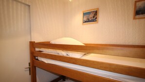 En våningssäng med vita sängkläder, en trägavel och en dörr till vänster.