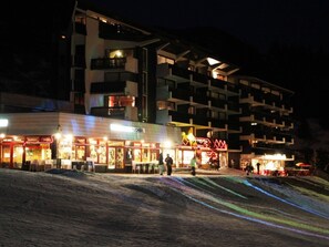 Ein mehrstöckiges Hotel mit Balkonen, ein Restaurant im Erdgeschoss und eine Skipiste im Vordergrund.