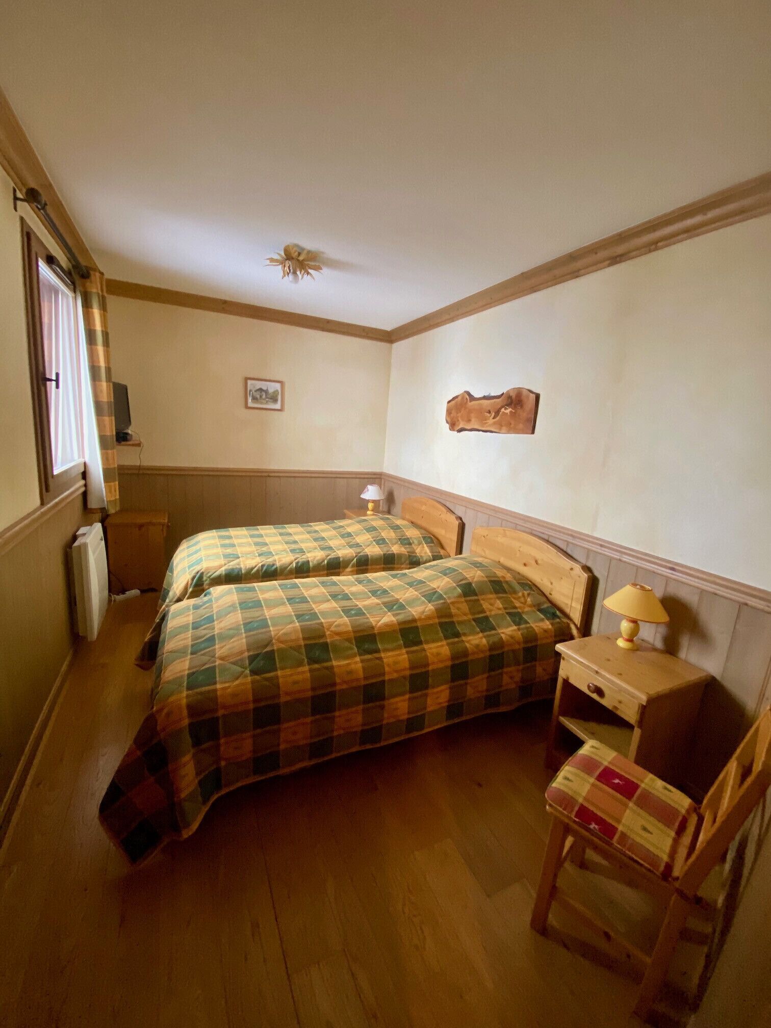 A small, cozy bedroom with two beds, a wooden nightstand, a chair, and a radiator.