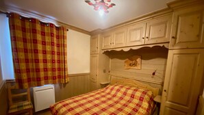 Un dormitorio con cama, armarios de madera, un radiador y una ventana con cortinas.