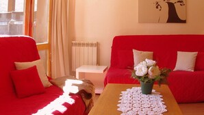 Een kamer met een rode bank, een houten bijzettafeltje met een kant kleedje en een witte radiator.