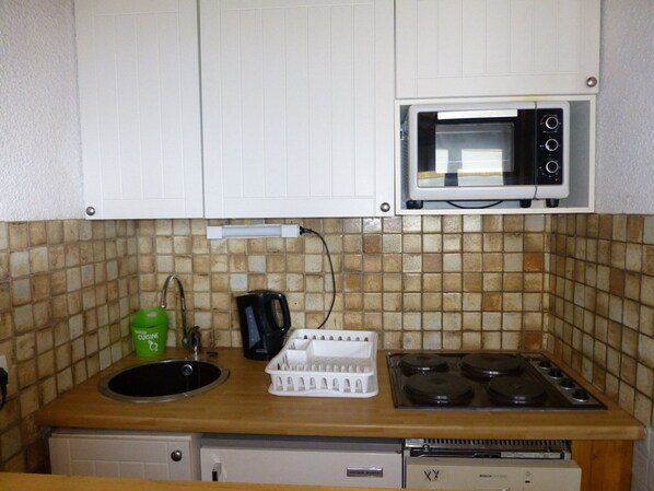 A compact kitchen with a microwave, stove, sink, and a small dishwasher. - Cozy Studio for 4, Close to Slopes & Shops - Alpe d'Huez, 2nd Floor Balcony, Ski Locker, No Pets (Huez)