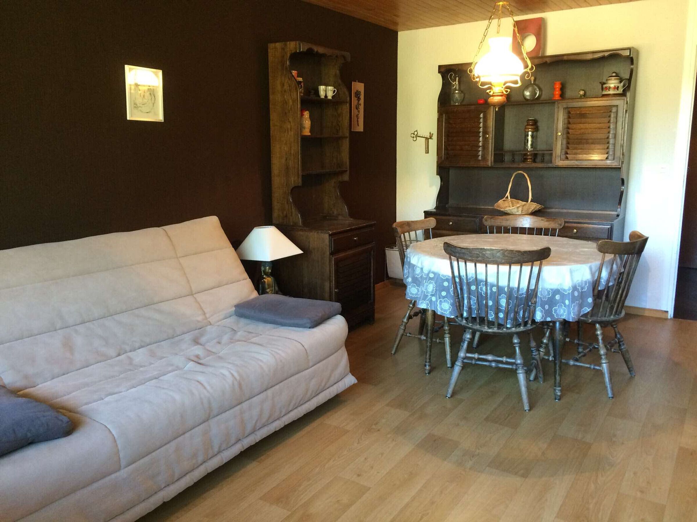 Un salon comprenant un canapé, une table à manger avec des chaises, un meuble en bois et un luminaire suspendu.
