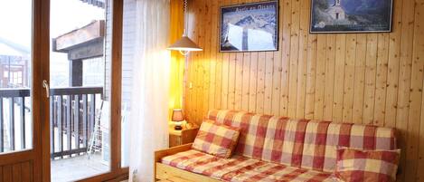 A wooden cabin with a sofa, a table, and a window with curtains.