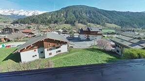 Ein Bergdorf mit traditionellen Holzhäusern, blauem Himmel und schneebedeckten Bergen im Hintergrund.