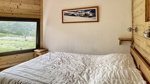 A bedroom with a large window, a bed, a wooden headboard, and a framed picture on the wall. - Modern duplex, ski-in/ski-out, south balcony (Les Menuires)