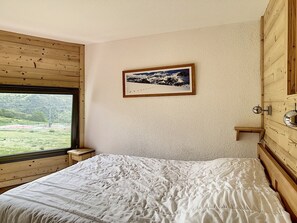 A bedroom with a large window, a bed, a wooden headboard, and a framed picture on the wall.