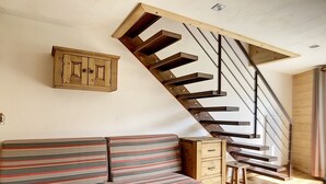 A modern interior with a wooden staircase, a striped sofa, and a small wooden cabinet. - Modern duplex, ski-in/ski-out, south balcony (Les Menuires)