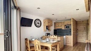 A modern kitchen with wooden cabinets, a dining table with chairs, and a TV mounted on the wall. - Modern duplex, ski-in/ski-out, south balcony (Les Menuires)