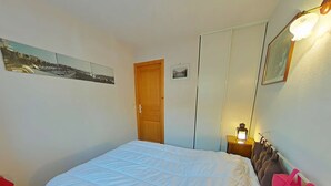 Ein Schlafzimmer mit einem Bett, einer Holztür, einem Nachttisch mit Lampe und zwei gerahmten Bildern an der Wand.