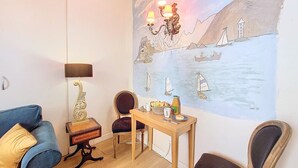 A cozy room with a blue sofa, a wooden table with a lamp, and a wall mural of a coastal scene.