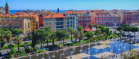 A square plaza with fountains, surrounded by colorful buildings and palm trees.