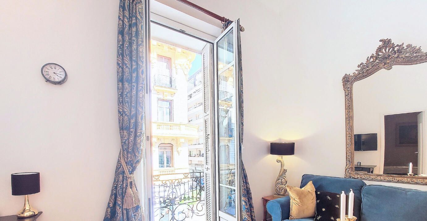 A living room with a blue sofa, a large ornate mirror, and a view of a building through a glass door.
