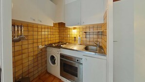 A compact kitchen with a washing machine, oven, and a sink. - Cozy 2-Room Apartment with Mountain Views, Near Village Center and Ski Trails - Sleeps 4 (Le Grand-Bornand)