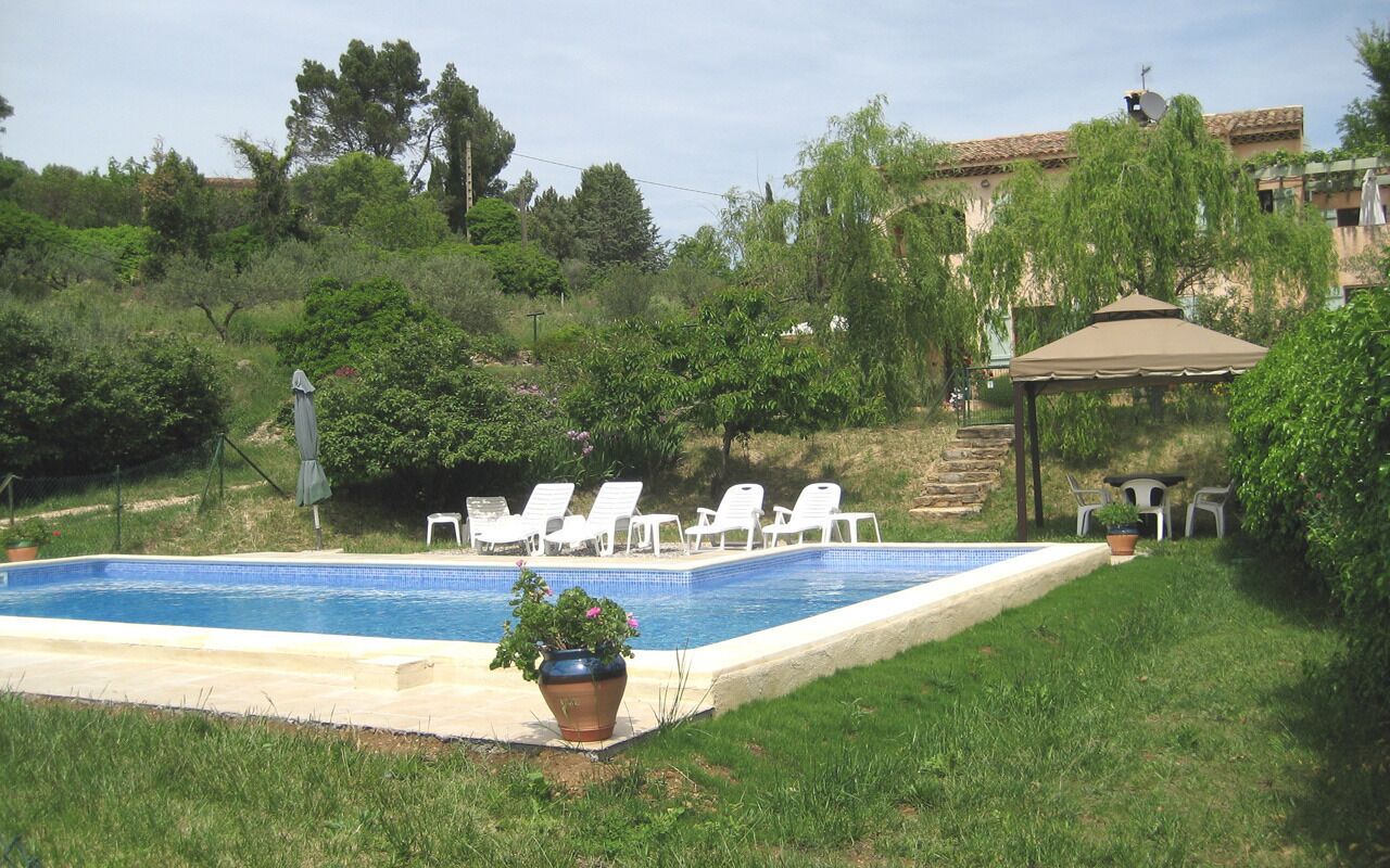 A swimming pool with lounge chairs, a gazebo, and surrounding greenery.