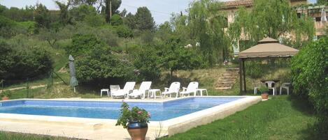 A swimming pool with lounge chairs, a gazebo, and surrounding greenery.