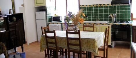 A kitchen with a dining table, chairs, and a vase of flowers. There is a refrigerator, microwave, and stove.
