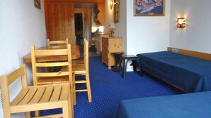 A room with a wooden table and chairs, a bed with a blue bedspread, a dresser, and a painting of a mountain on the wall. - Ski-in studio, 4 pax, pets allowed - Les Arcs 1800 (Les Arcs 1800)