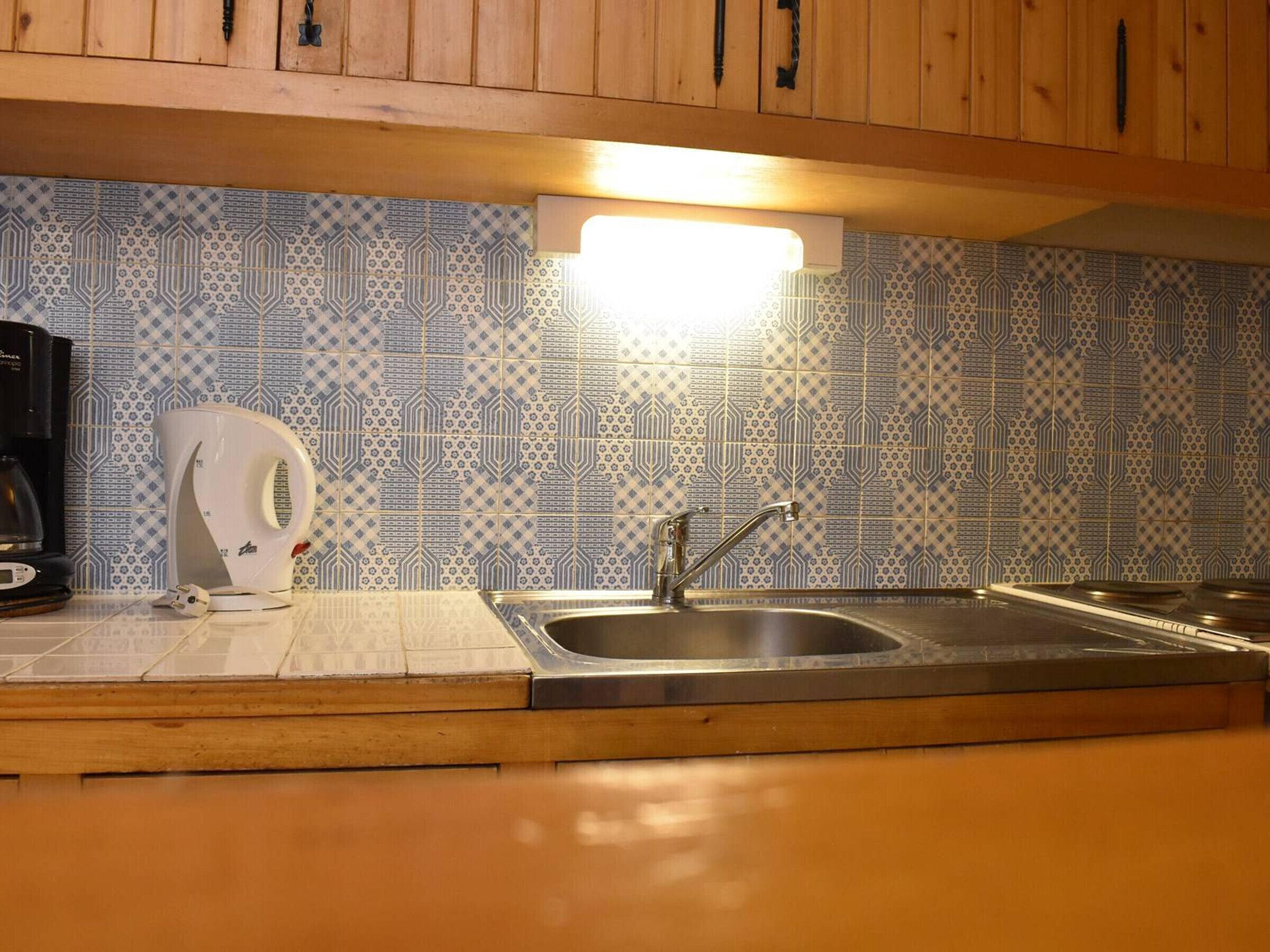 A kitchen with a patterned backsplash, a stainless steel sink, and wooden cabinets.