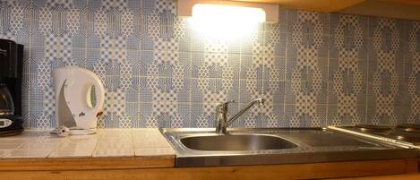 A kitchen with a patterned backsplash, a stainless steel sink, and wooden cabinets.
