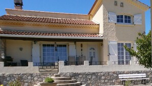 Un edificio de dos pisos con techo de tejas, paredes de piedra y un balcón con mobiliario exterior.