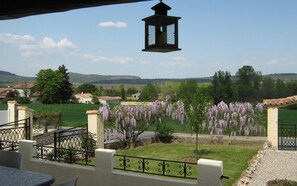 A patio with outdoor seating, a view of a garden with purple flowers, and a distant landscape with houses and hills. - Valerie Talo Mazaugues (MAZAUGUES)