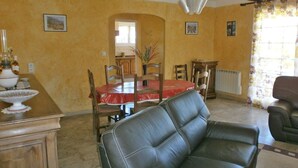 Un comedor con una mesa roja, sillas y un florero. Se observa un mueble de madera y un sofá de cuero negro.