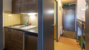 A compact kitchen with wooden cabinets, a stainless steel refrigerator, and a sink with a dish rack. - Cozy 5-person studio near slopes, parking included (La Mongie)