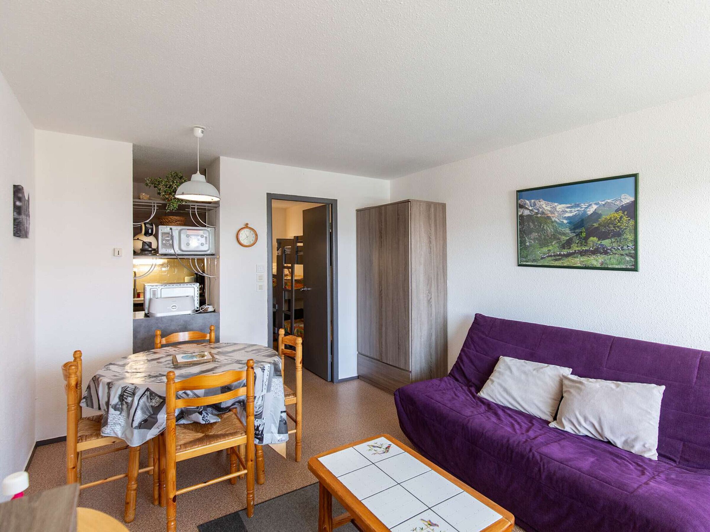 Un espacio habitable compacto con comedor, un sofá morado y una cocina al fondo.