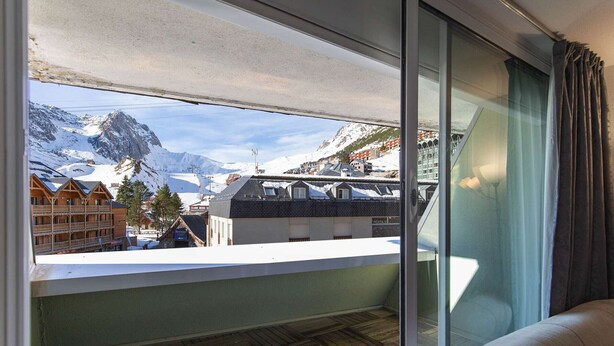 A balcony with a view of snow-covered mountains and a ski resort. - Cozy 5-person studio near slopes, parking included (La Mongie)