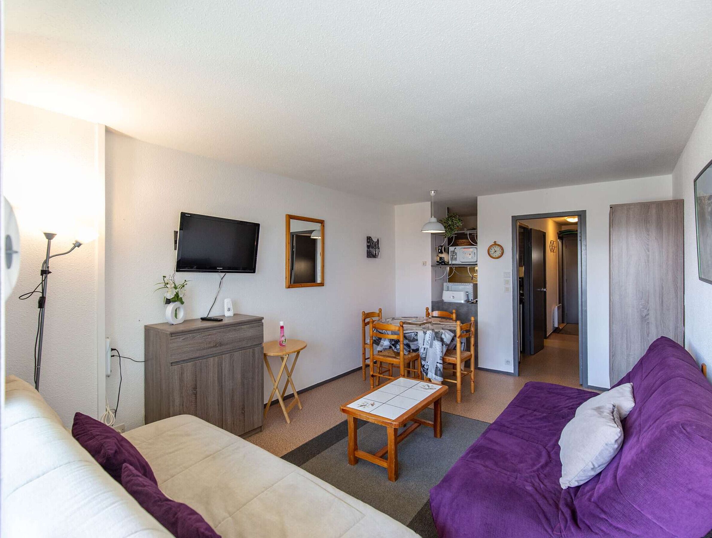 Un espace de vie compact comprenant un canapé, une petite table à manger, un téléviseur et une kitchenette.