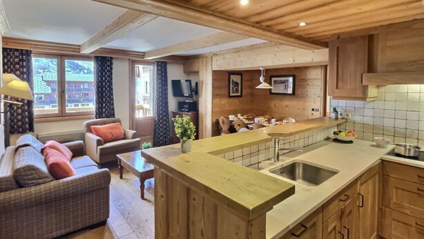 Een ruime woonkamer met een bank, een eettafel en een keuken met houten kastjes en een groot kookeiland.