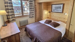 Een kamer met houten lambrisering, een bed, een bureau, een lamp en een raam met gordijnen.
