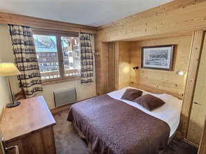 A wooden room with a bed, a desk, and a window with curtains.