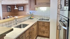 Een keuken met houten kastjes, een dubbele spoelbak, een kookplaat en een betegelde achterwand.