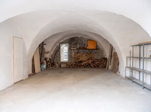 Una stanza mansardata con soffitto spiovente, una porta in legno, una finestra, un muro in pietra e uno scaffale in metallo.