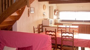 Ein gemütliches Zimmer mit einer Holztreppe, einem Esstisch mit Stühlen, einer Küchenzeile mit einer Mikrowelle und einem Bett mit rosa Bettwäsche.