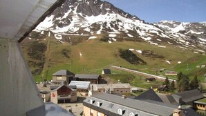 Un pueblo de montaña con una vía de tren, edificios de arquitectura tradicional y montañas nevadas al fondo.