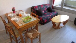 Un comedor con una mesa y sillas de madera, un sofá floral y una ventana con cortinas.