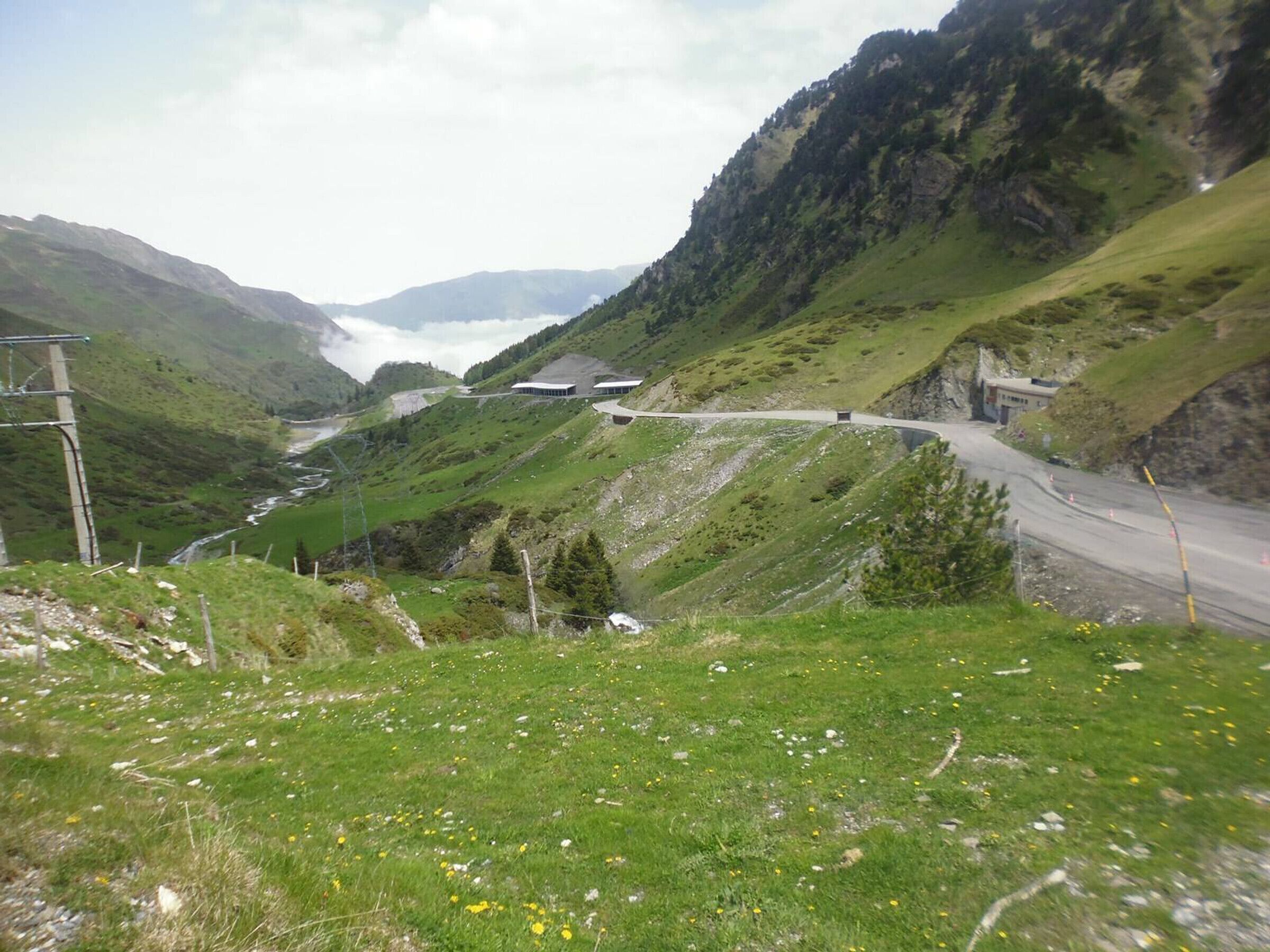 Een bergachtig landschap met een slingerende weg, een klein gebouw en een rivier in de vallei.