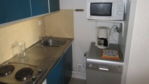Una kitchenette compacta equipada con estufa a gas, lavamanos, microondas y cafetera.