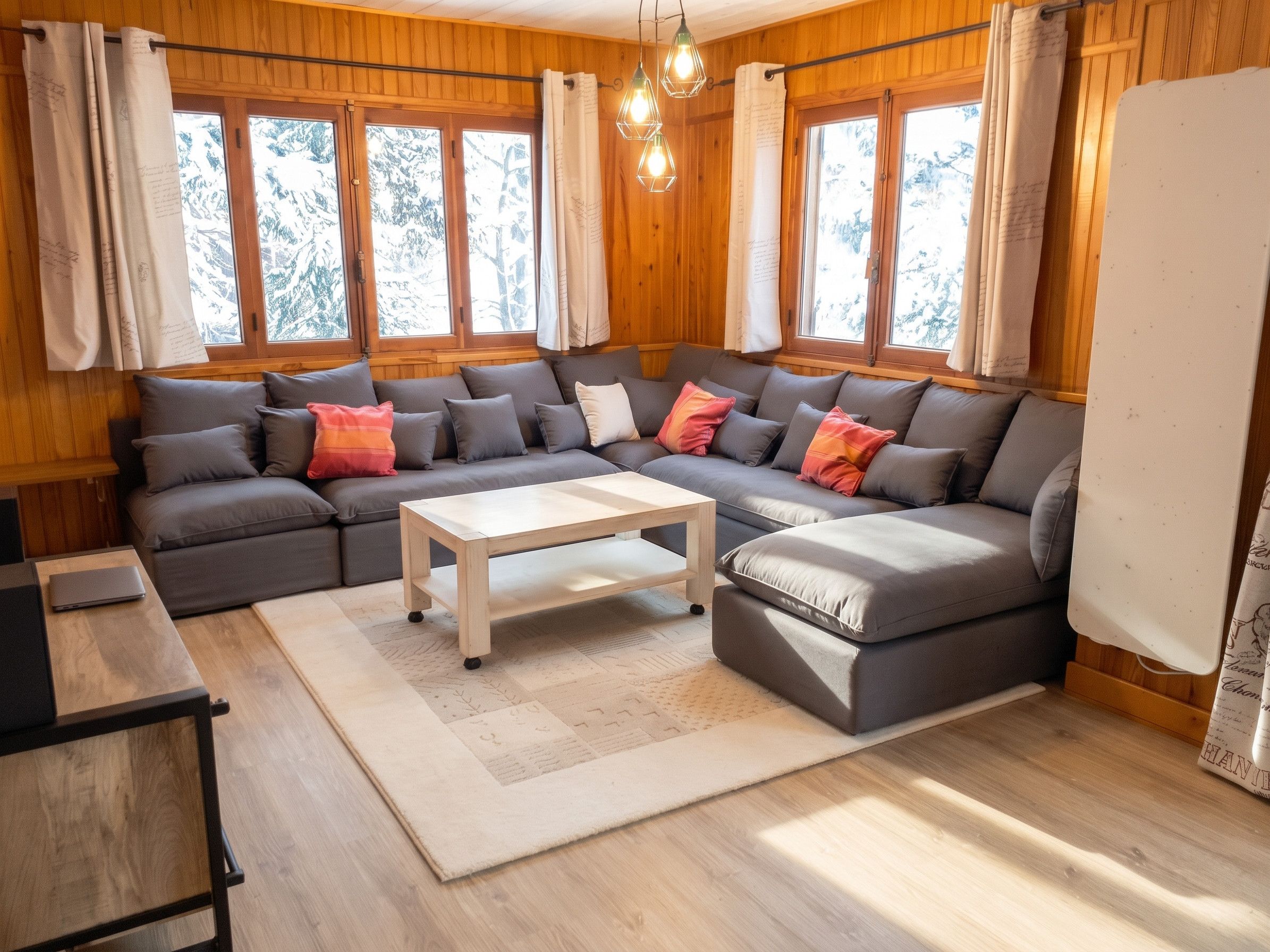 A cozy living room with a sectional sofa, a coffee table, and a laptop on a side table.