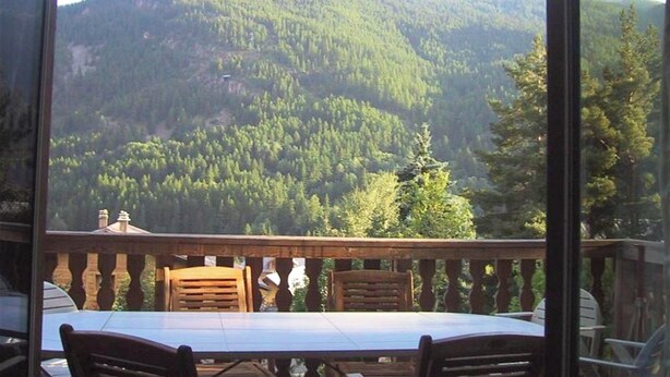 A balcony with a table and chairs, overlooking a forested mountain. - Homerez - Chalet in Saint-Chaffrey, mountain view (Saint-Chaffrey)