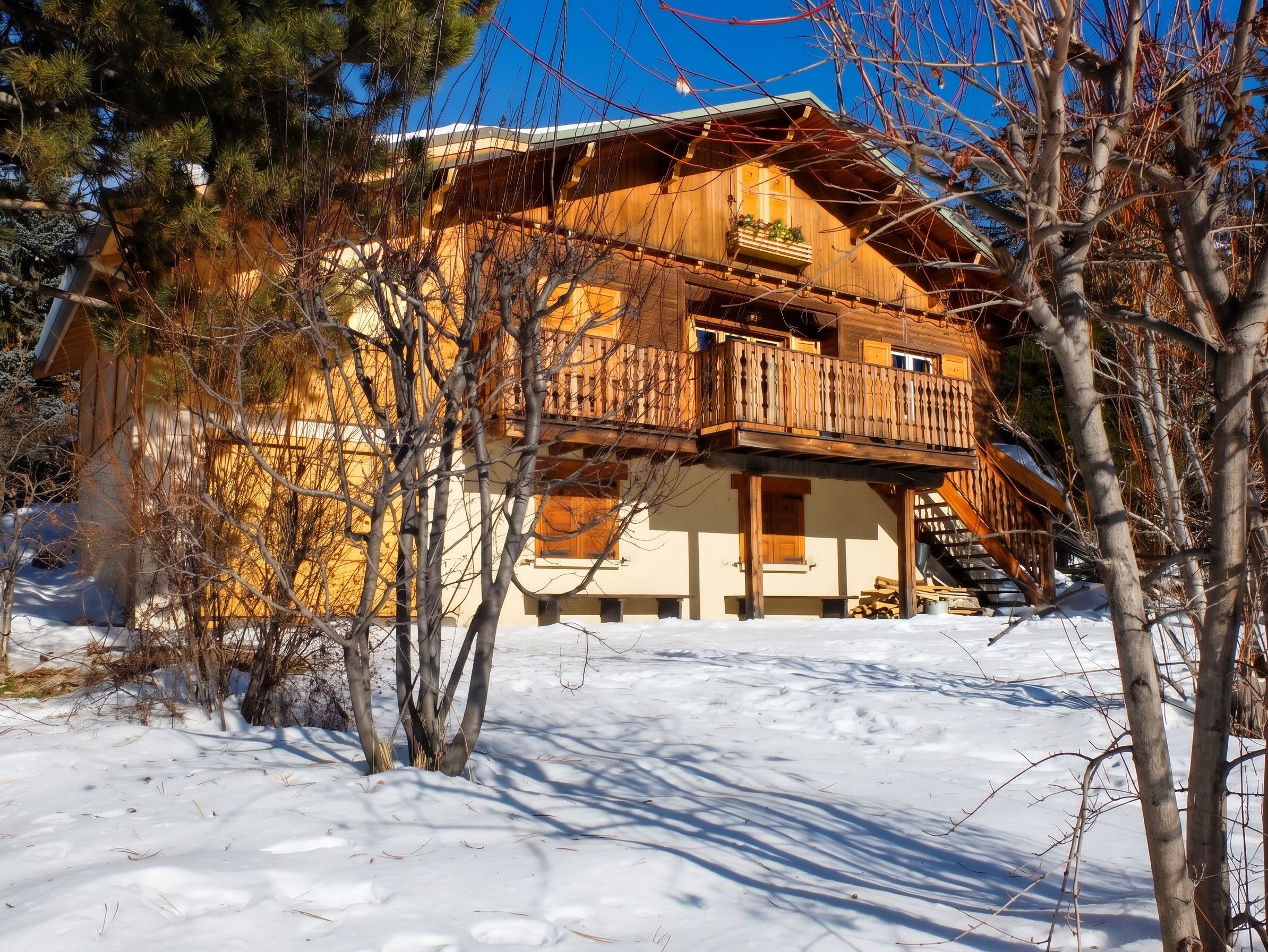 Eine Holzchalet mit Balkon, umgeben von Schnee und kahlen Bäumen.